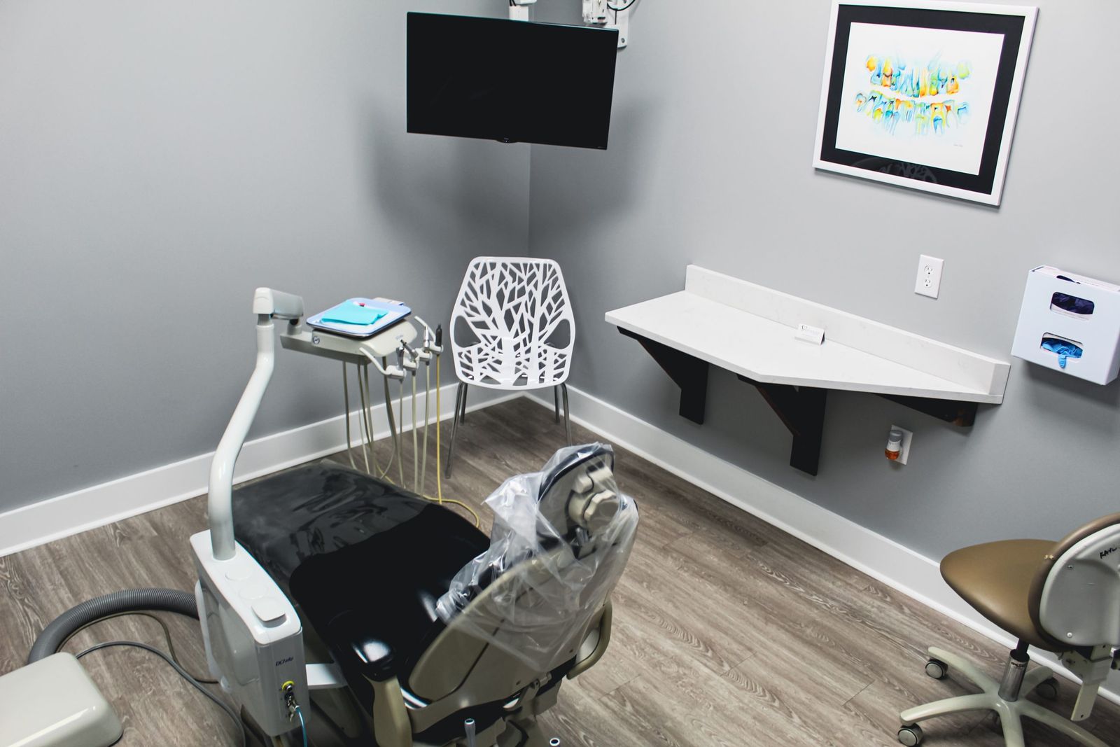 A treatment room with a dental chair and a ceiling-mounted screen