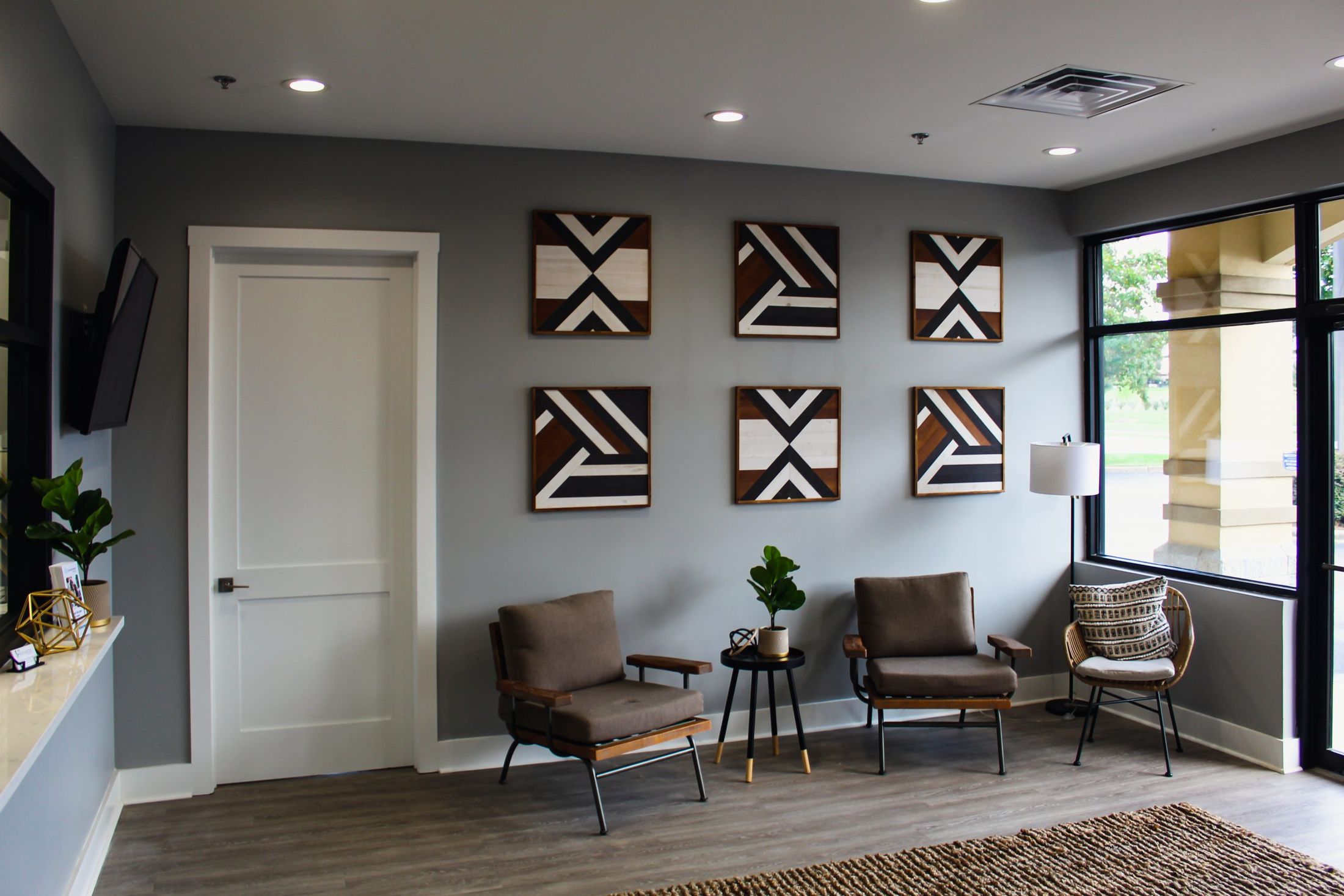 The waiting room at Advanced Dental Clinic, with geometric wood art on a grey wall and seating by the window